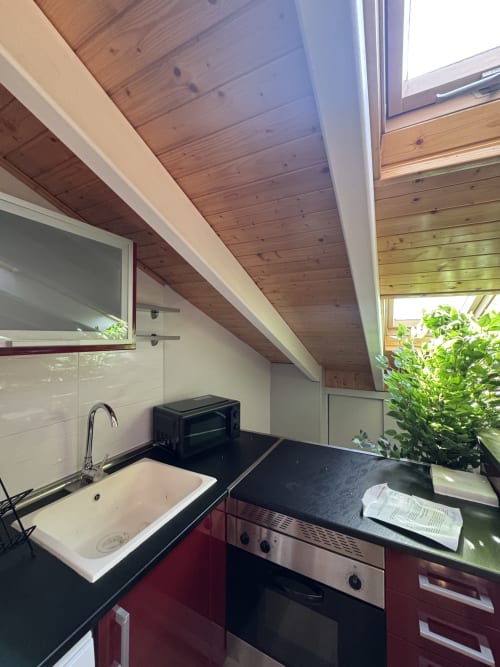 Moderna cocina ático en Madrid con techo de madera, armarios rojos, encimera negra y vistas a la ciudad