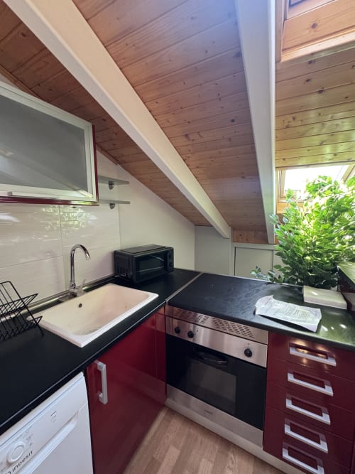 Cocina moderna en ático con muebles burdeos, encimeras negras, techo de madera y vistas a la ciudad en apartamento madrileño