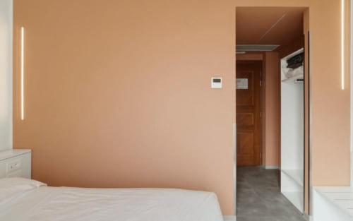 Modernes Hotelzimmer in Ca'Tron in Dolo mit Pfirsichfarbenen Wänden, weißem Bett und minimalistischen Leuchten