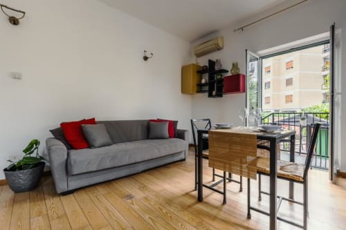 Soggiorno moderno a Luxury Trevi House Roma con divano grigio, tavolo da pranzo e balcone con vista sulla città