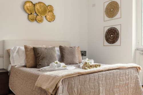 Camera da letto lussuosa a Trevi House Roma con biancheria beige elegante, decorazioni dorate alle pareti e cuscini texturizzati