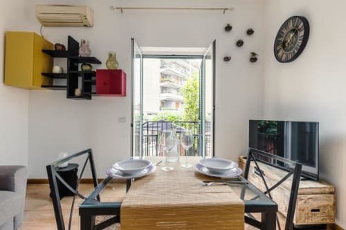 Zona pranzo moderna della Luxury Trevi House Roma con tavolo apparecchiato, vista dal balcone, opere d'arte e TV a schermo piatto