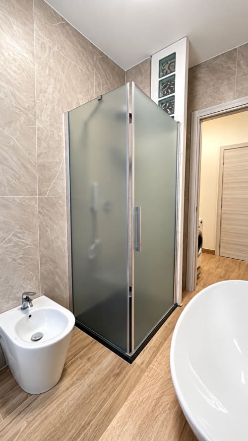 Bagno moderno a Tolstoi 13.15 con box doccia in vetro satinato, lavabo bianco a colonna e pavimento in legno a Saronno