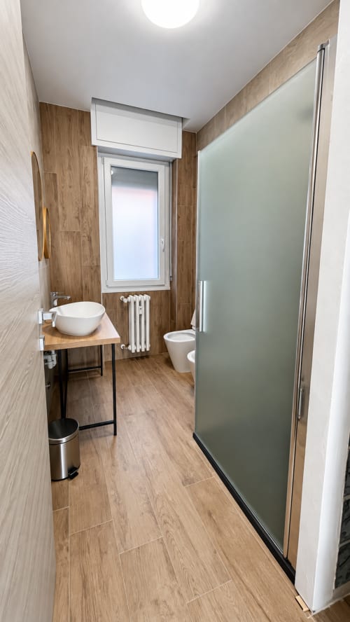 Bagno moderno a Tolstoi 13.15 Saronno con pavimento in legno, lavabo rotondo, wc e doccia con vetro satinato