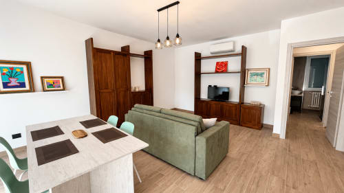 Zona living moderna a Tolstoi 13.15 a Saronno con tavolo da pranzo, divano verde, scaffali in legno e illuminazione a sospensione