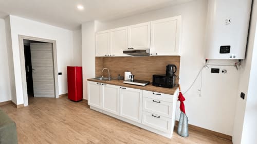 Moderna cucina nell'appartamento Tolstoi 13.15 a Saronno, con mobili bianchi, piano in legno, lavello in acciaio e elettrodomestici.