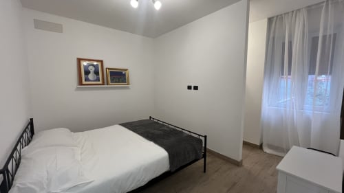 Camera da letto moderna nell'appartamento Tolstoi 13.15 a Saronno con letto a struttura nera, biancheria bianca e vista sulla città attraverso le tende