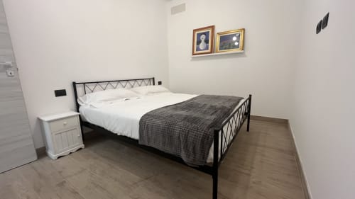 Camera da letto spaziosa nell'appartamento Tolstoi 13.15 a Saronno con letto in metallo nero, biancheria bianca, coperta grigia e comodino