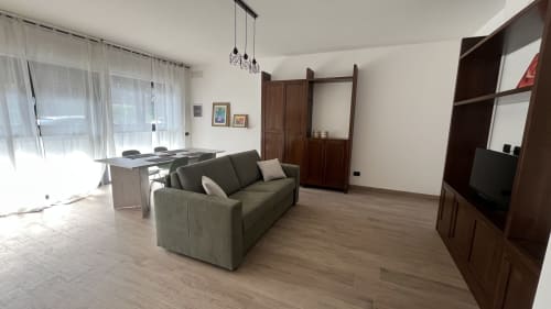 Moderno appartamento a Tolstoi 13.15 a Saronno con divano verde, zona pranzo, scaffalature in legno e vista sulla città
