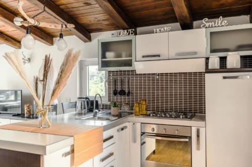 Cucina moderna a Luxury Trevi House Roma con mobili bianchi, rivestimento in piastrelle nere, travi in legno e decorazioni di erbe pampas