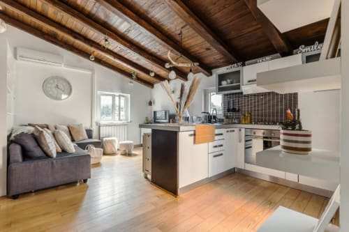 Cucina open-plan moderna con travi in legno a vista, arredamento bianco e zona soggiorno accogliente al Luxury Trevi