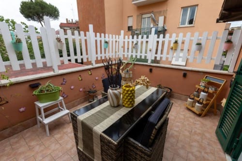 Terrazza della lussuosa Trevi House Roma con tavolo da pranzo, recinto bianco, piante in vaso e pavimenti in cotto