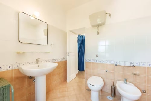 Bagno luminoso nell'appartamento B&B Oliveri 25 Procida con lavabo su piedistallo, WC, bidet e doccia con tenda blu