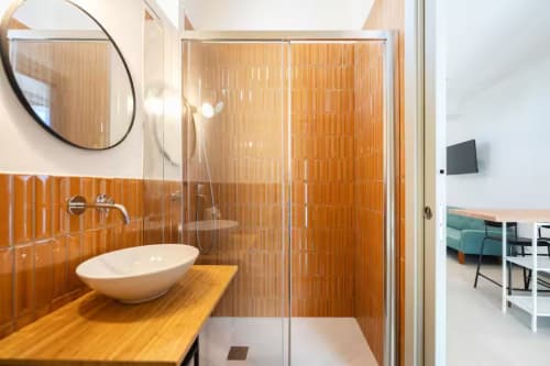 Bagno moderno in B&B Oliveri 25, Procida con piastrelle arancioni, lavabo rotondo, box doccia in vetro e specchio circolare