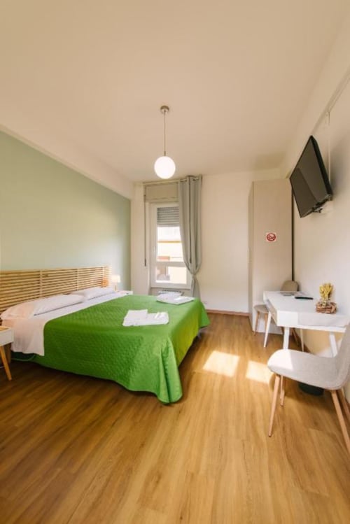 Camera moderna e luminosa presso Provincia di Verona B&B con coperta verde, pavimento in legno, scrivania, TV e vista sulla corte interna