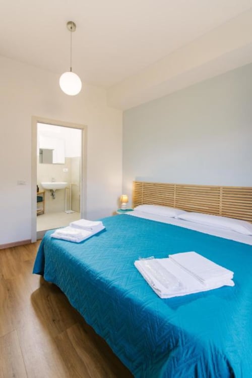 Camera moderna al lago presso Provincia di Verona B&B con biancheria azzurra, testata in legno, bagno privato e elegante lampada a sospensione