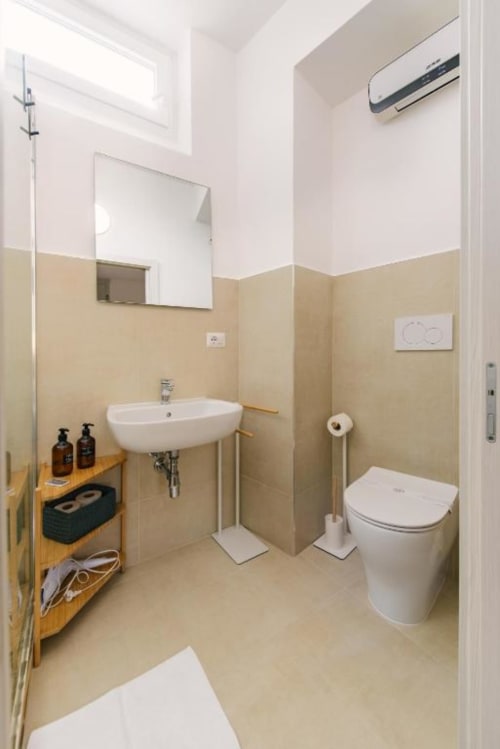 Bagno moderno nella Lake Room di Provincia di Verona B&B con water bianco, lavabo curvo, piastrelle beige e aria condizionata