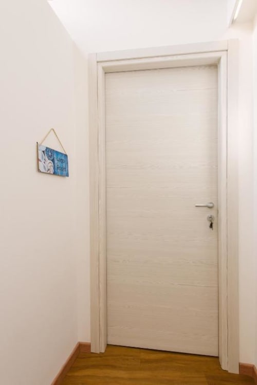 Minimalista porta in legno bianco con serratura nel corridoio della Lake Room presso Provincia di Verona B&B, con piccola opera d'arte blu sulla parete