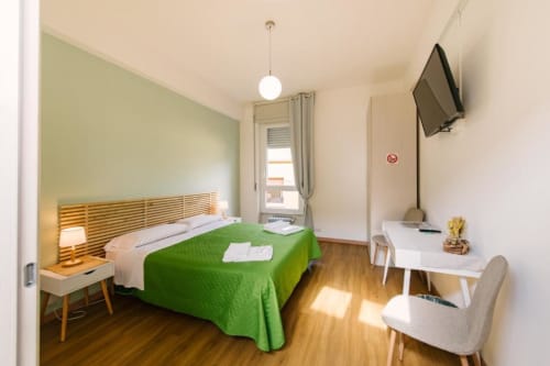 Camera luminosa con copriletto verde, testata in legno, scrivania, TV e vista sulla corte interna della Verona B&B