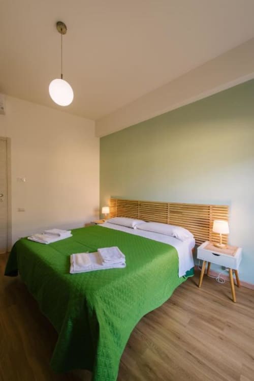 Camera Colli di Provincia di Verona B&B con coperta verde, testata in legno, lampada a sospensione e vista sulla corte interna