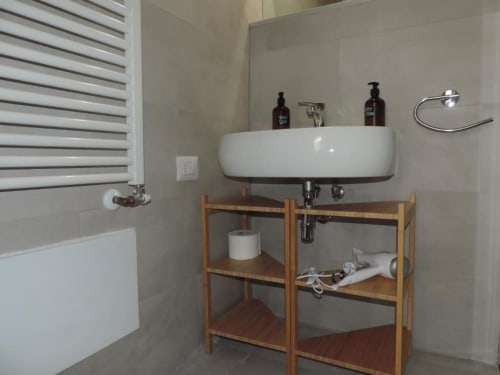 Bagno moderno nella Provincia di Verona con lavabo bianco, scaffali in legno e piastrelle beige