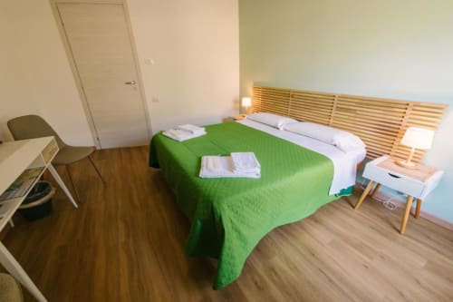 Accogliente camera nel B&B della Provincia di Verona con coperta verde, testata in legno, scrivania e pavimento in legno