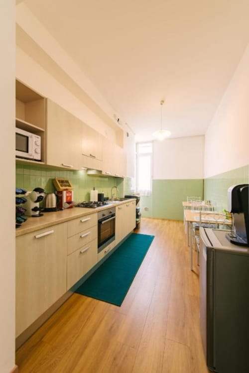 Cucina moderna in B&B a Verona con armadi color crema, rivestimento verde, pavimenti in legno e zona pranzo con vista sulla corte