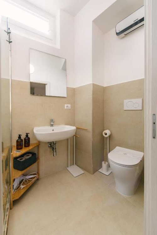 Bagno moderno in B&B a Provincia di Verona con piastrelle beige, lavabo bianco, WC e mensole in legno con amenities