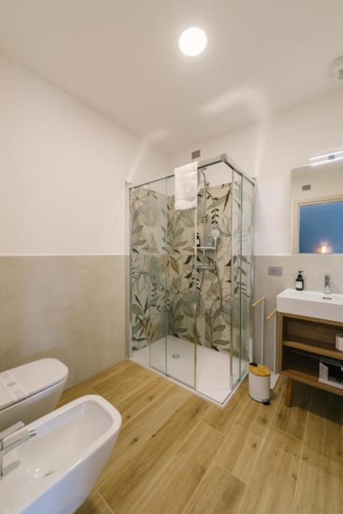Bagno moderno con doccia aperta, porte in vetro con motivi botanici, pavimento in legno, lavabo e wc bianchi presso Provincia di Verona B&B
