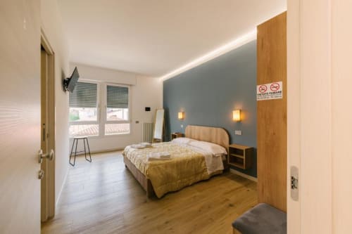 Camera da letto moderna con letto matrimoniale, parete azzurra, illuminazione calda, arredi in legno e ampie finestre nella Verona B&B