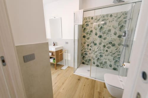 Bagno moderno presso il B&B Provincia di Verona a Verona con doccia in vetro, parete rivestita in piastrelle botaniche, mobile lavabo in legno e finiture bianche