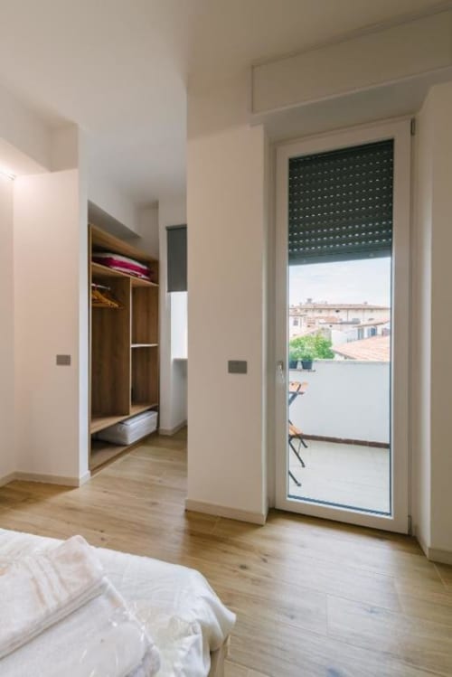 Camera moderna della B&B di Verona con pavimenti in legno, armadio aperto e balcone con vista sui monumenti