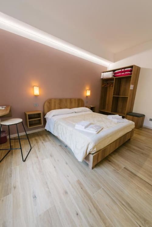 Camera moderna della guest house di Verona con letto in legno, biancheria bianca, pavimento in legno, pareti rosa e illuminazione ambient.