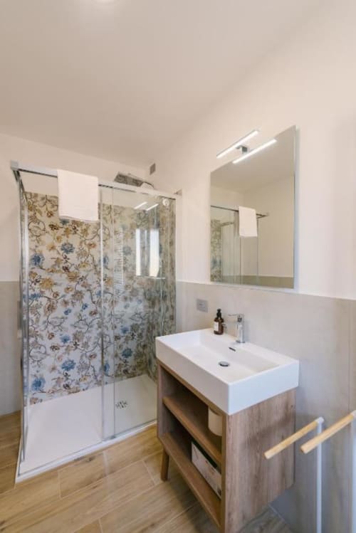 Bagno moderno nella B&B di Verona con lavabo bianco, mobile in legno, ampio specchio, illuminazione LED e doccia con decorazioni floreali