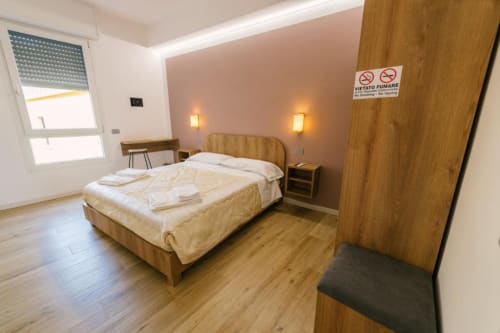 Camera matrimoniale moderna nella B&B di Verona con letto in legno, illuminazione calda, pavimentazione in legno e vista sulla città dalla finestra.