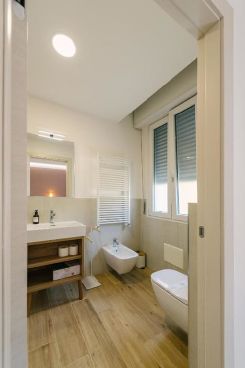 Bagno moderno nel B&B di Verona con lavabo bianco, WC, bidet, pavimento in legno, specchio e portasciugamani