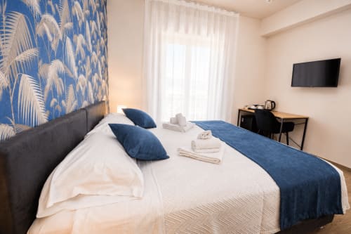 Camera Blu Palm al Le Rooms B&B di San Benedetto del Tronto con carta da parati a palme blu, letto bianco con cuscini blu, TV e vista sulla città