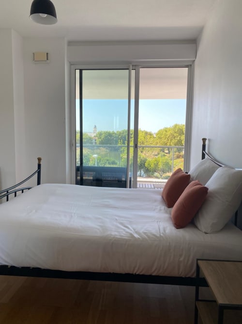Chambre moderne avec literie blanche, balcon vue sur le lac de La Rochelle, lampadaire noir et design contemporain