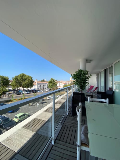 Balcon d'appartement moderne avec terrasse en bois, vue sur la ville de La Rochelle, mobilier confortable et bâtiments historiques en arrière-plan