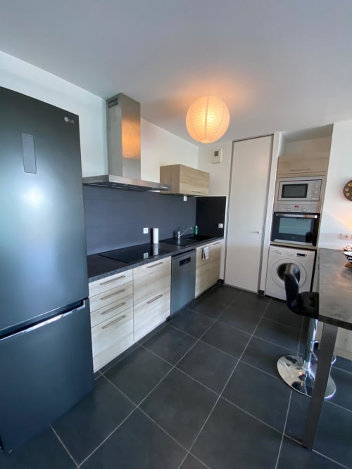 Cuisine moderne de l'appartement La Parenthèse à La Rochelle avec plans de travail noirs, meubles en bois clair et acier inoxydable