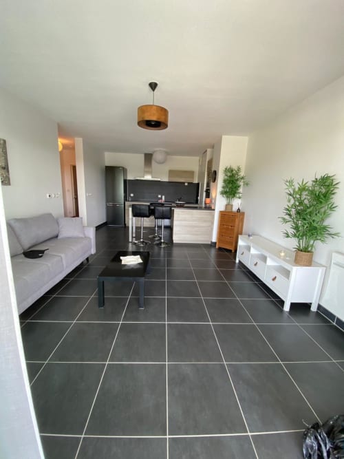 Séjour moderne ouvert dans un appartement à La Rochelle avec carrelage foncé, canapé gris, cuisine et espace salle à manger