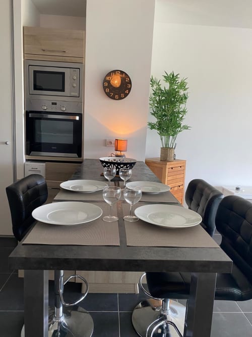 Salle à manger contemporaine dans l'appartement de La Rochelle avec table dressée, chaises noires, électroménagers intégrés et plantes décoratives
