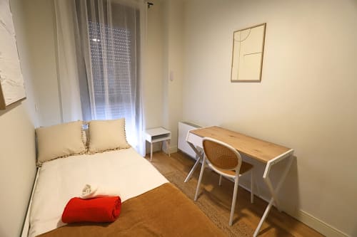 Habitación moderna en Madrid Río con cama individual, escritorio de madera, silla, ventana con visillos y decoración minimalista
