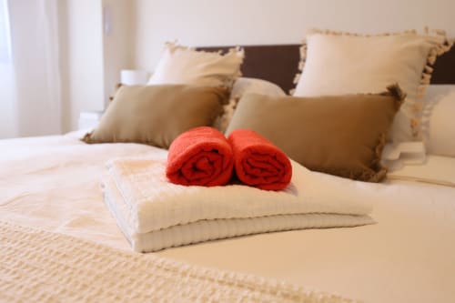 Toallas rojas enrolladas elegantemente sobre ropa de cama crema en un moderno apartamento madrileño con almohadas decorativas