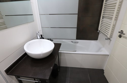 Baño moderno en apartamento de Madrid Río con lavamanos redondo blanco, tocador negro, bañera y acabados cerámicos contemporáneos