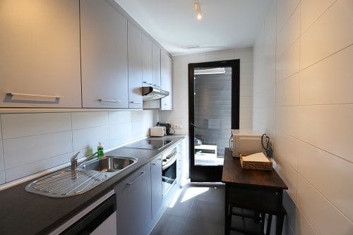 Cocina moderna en apartamento de Madrid Río con muebles blancos, encimeras negras, electrodomésticos de acero inoxidable y mesa de comedor