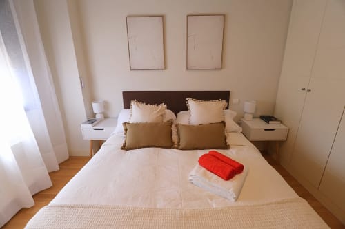 Dormitorio moderno en Madrid Río con cama queen, cabecero marrón, almohadas beige y toallas rojas sobre el colchón