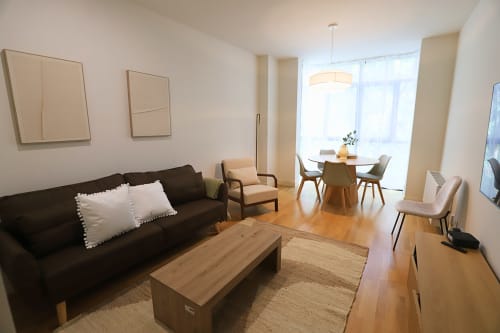 Apartamento moderno en Madrid Río con sofá negro, muebles de madera, comedor y ventanales hasta el techo