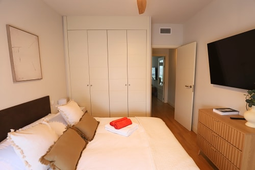 Dormitorio moderno en Madrid Río con cama queen, armarios empotrados, TV, cómoda de madera y diseño minimalista