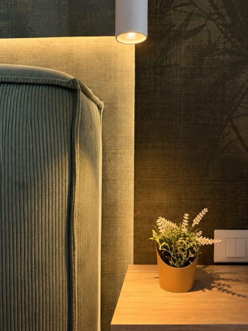 Angolo della suite moderna di Domus Fysi Palermo con poltrona verde, illuminazione ambientale e pianta in vaso sulla scrivania in legno